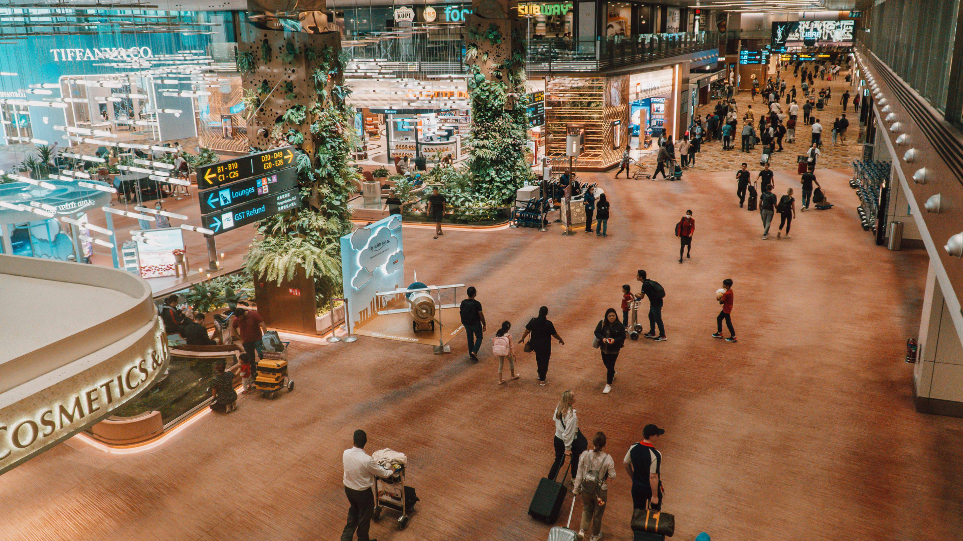 Modern luxury duty-free shopping in Changi Airport departure transit hall with high ceilings and gold-toned architectural lighting.